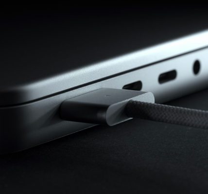 Close-up view of a braided charging cable (possibly MagSafe 3 or USB-C) connected to the side port of a laptop.