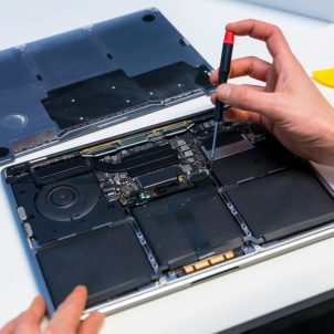 Repairing a laptop: A hand with a screwdriver is shown working on the inside of a MacBook with the bottom panel removed, revealing the internal parts.